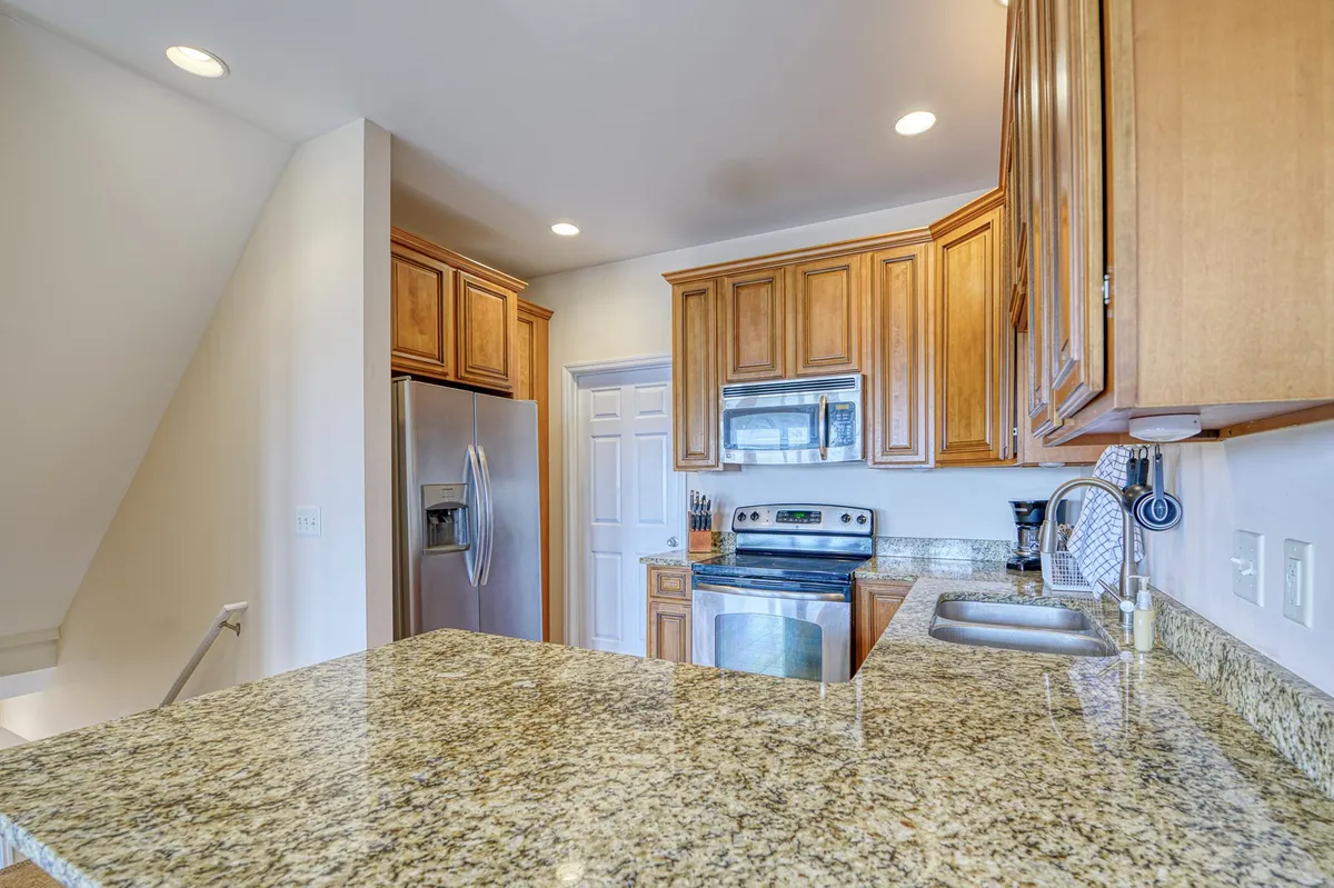 A modern kitchen with granite countertops, wood cabinetry, and stainless steel appliances, set up for both cooking and entertaining. The room exudes a welcoming vibe perfect for family meals or group gatherings.