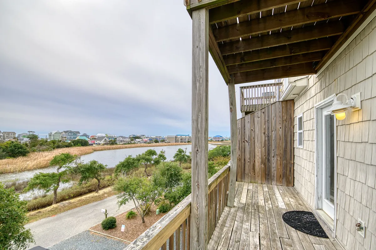 A wide view from a wooden deck overlooking tranquil water surrounded by lush marsh vegetation. The sky is cloudy, creating a soft, coastal atmosphere, and the deck provides a seamless transition between indoor comfort and the outdoors—an ideal spot for relaxing with your dog or watching them play nearby.