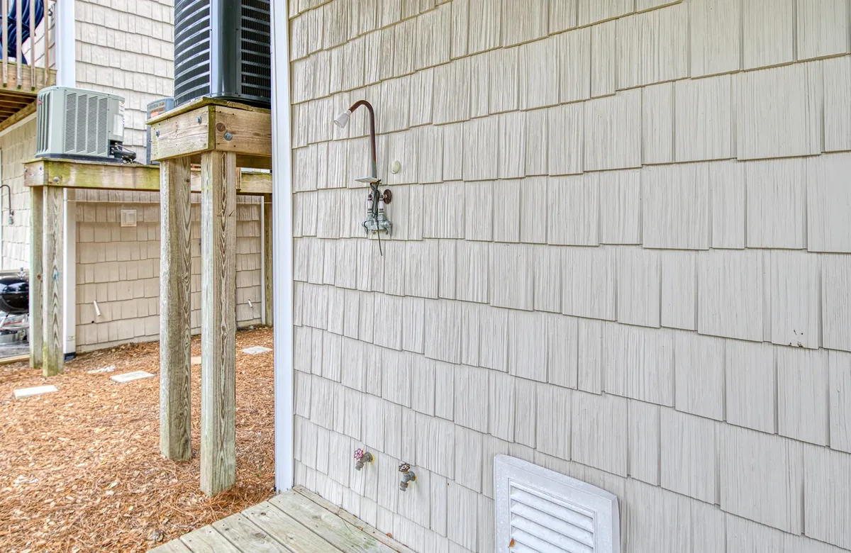 This image features an outdoor shower fixture mounted on a wooden deck wall, with a textured backdrop, embodying the informal and refreshing vibe of rinsing off after a day at the beach.