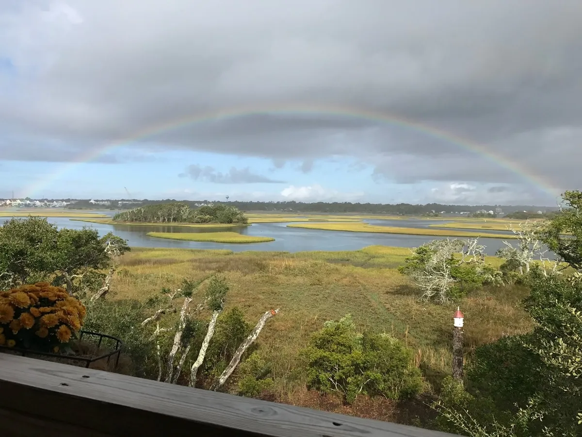 A panoramic view of marshland with a rainbow arching over the water, set against a backdrop of trees. This tranquil scene highlights the natural beauty and wildlife of the area, reinforcing the appeal of the property’s location for couples seeking peaceful exploration and memorable moments.