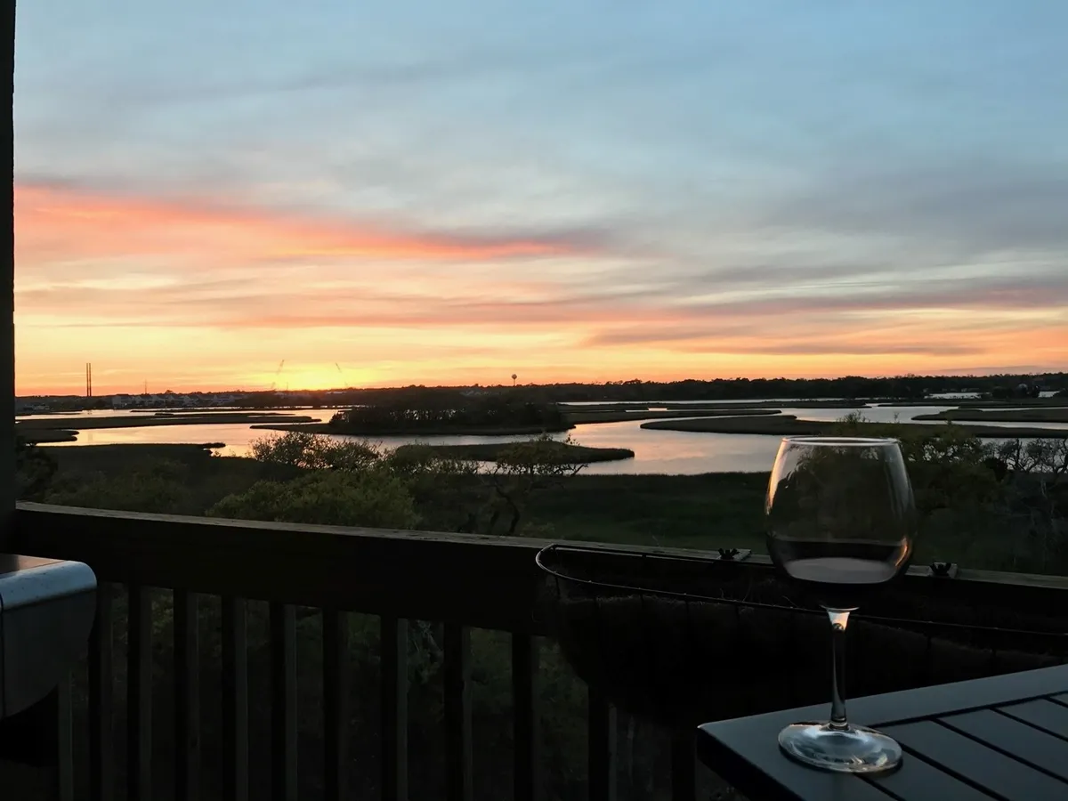 A stunning sunset scene over the water, with a glass of wine in the foreground and lush greenery surrounding meandering waterways. The ambiance is peaceful and intimate, evoking romantic evenings spent savoring the view and each other's company.