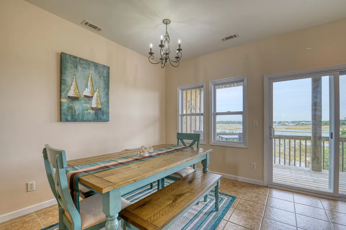 A welcoming dining area with a large table, modern chandelier, elegant artwork, and bright windows that provide views of the surrounding scenery. The setup is ideal for family dinners, celebrations, or game nights with friends.
