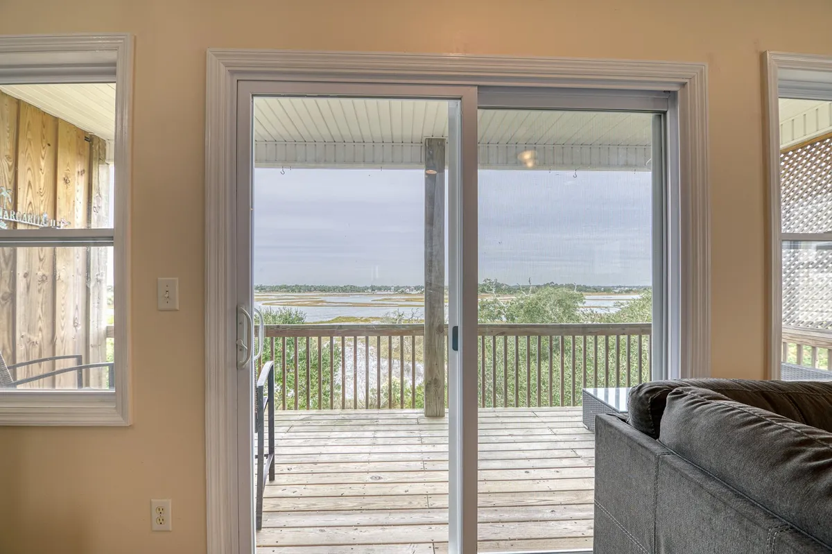 An exterior view from a private outdoor deck with a sliding glass door, offering a sweeping vista of the surrounding landscape. The space is set up for relaxation, inviting guests to enjoy the tranquil setting and scenic water views. The deck is ideal for morning coffee or evening cocktails, making it an appealing spot for couples seeking privacy and connection to nature.
