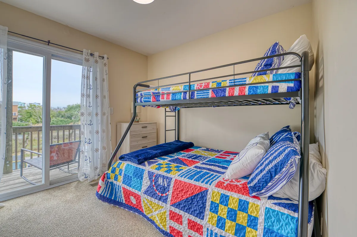 A cheerful, cozy bunkroom with a bright window, colorful bedding, and a bunk bed that's perfect for kids or families. The room feels inviting and playful, with ample daylight and a view outside, making it a welcoming nook for younger guests.
