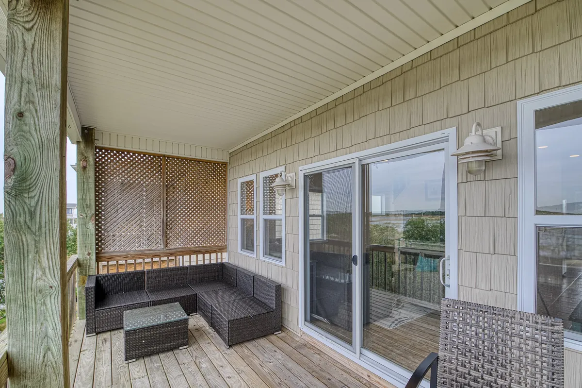 The image captures a welcoming outdoor seating area on a wooden deck, complete with inviting chairs and sliding glass doors that connect the interior to the exterior living space. Morning or evening light enhances the relaxed mood.